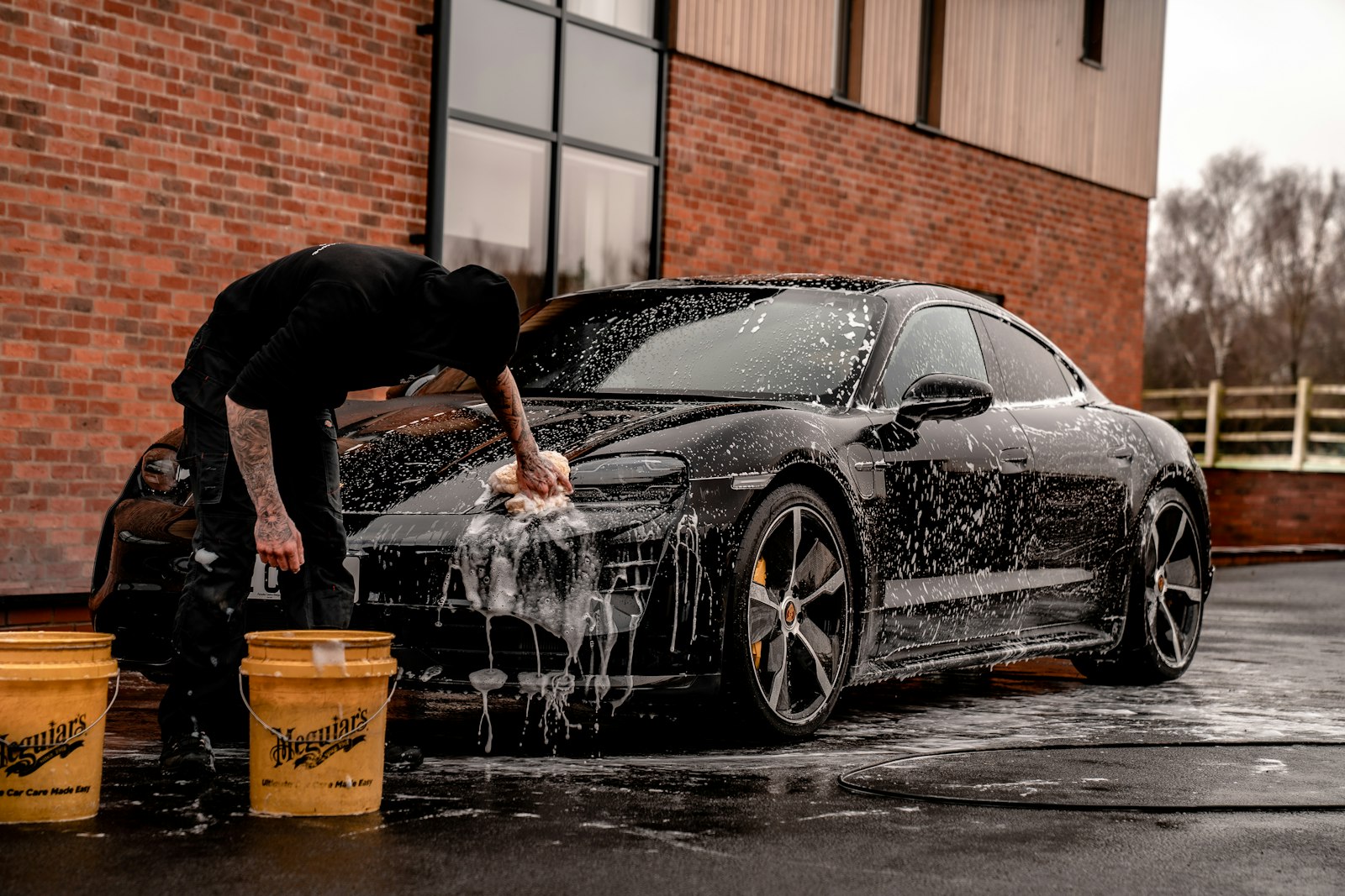 A dark car covered in soap suds being washed by hand with a wash mitt